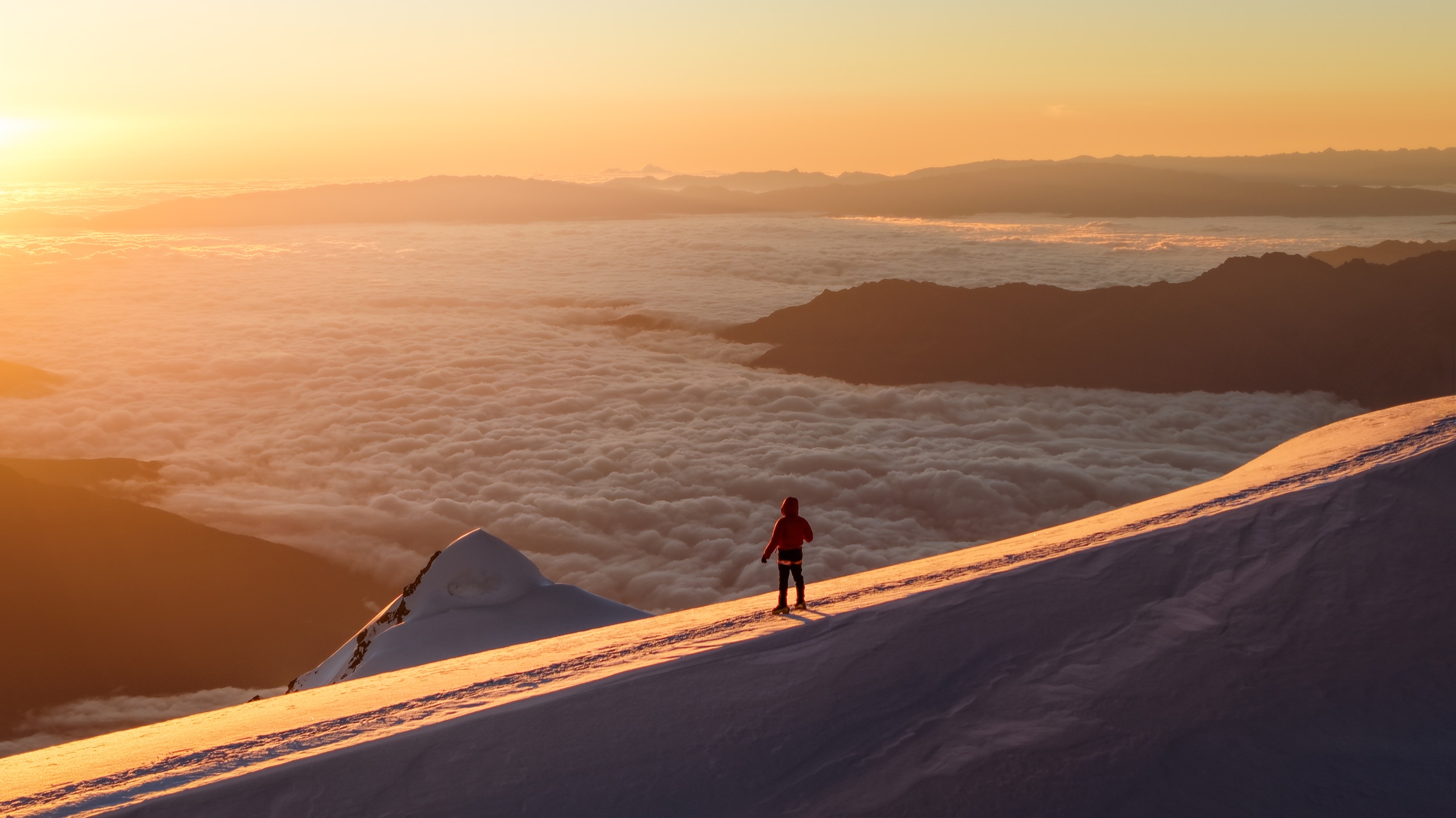 A mountaineer standing on a snowy ridge above the clouds at sunset