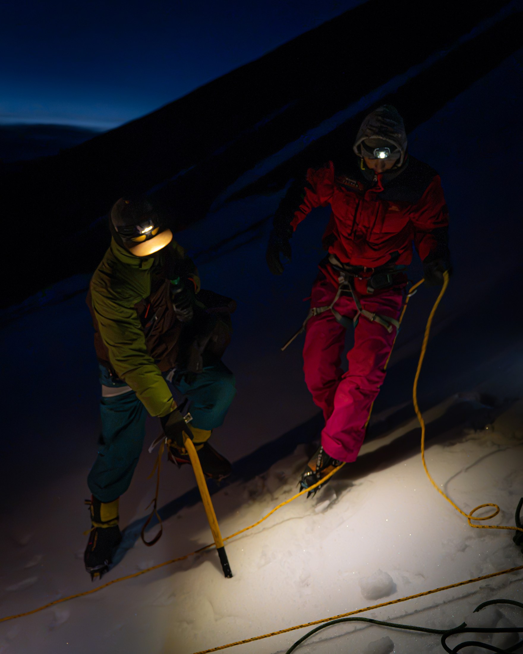 Two climbers with ice axes and headlamps on Kaigar Ri before dawn